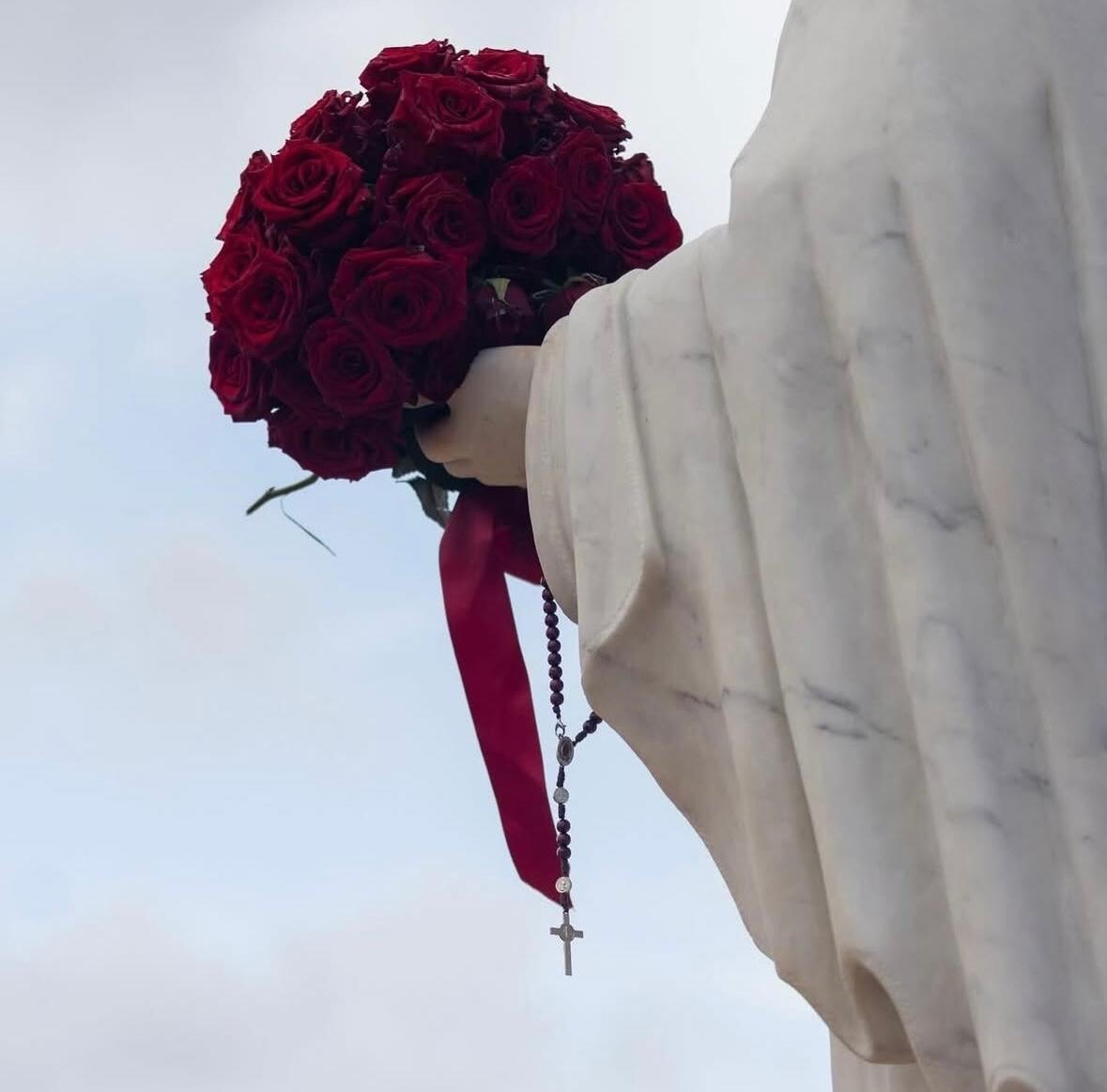 Bouquet de roses rouges et chapelet tenus dans la main de la statue de la Vierge